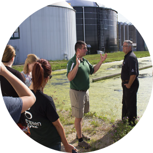 A photo of MSU employee Dana Kirk speaking to several students in front of the South Campus Anaerobic Digester. 