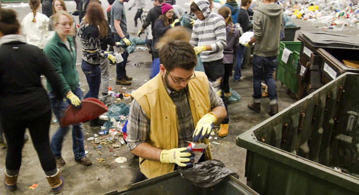 A student in gloves sorts waste into different containers.