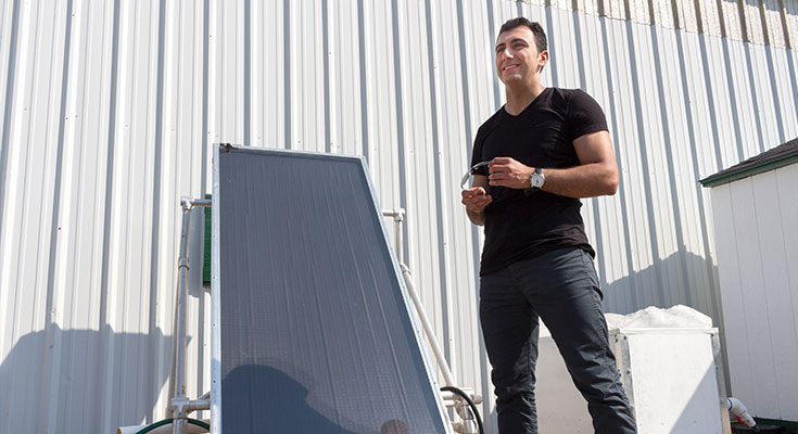 Sina Jahangiri posing near a flat plate collector system for solar water heating. A flat plate collector looks similar to traditional solar panels and consists of a dark flat-plate with an aluminum border.