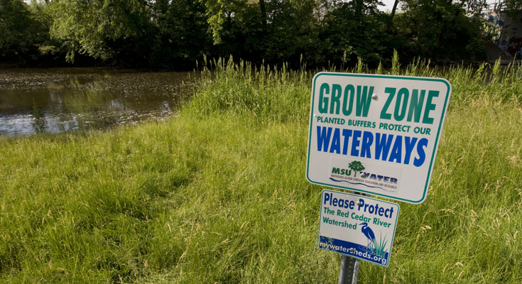 A photo of the Red Cedar River shoreline, with a waterways protection sign in the foreground.