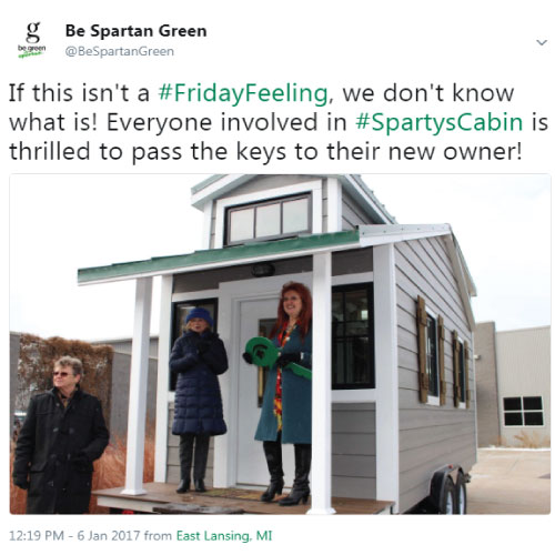A screenshot of a tweet by @BeSpartanGreen, displaying a photo of the key passing ceremony for Sparty's Cabin, a tiny house built by MSU students. 