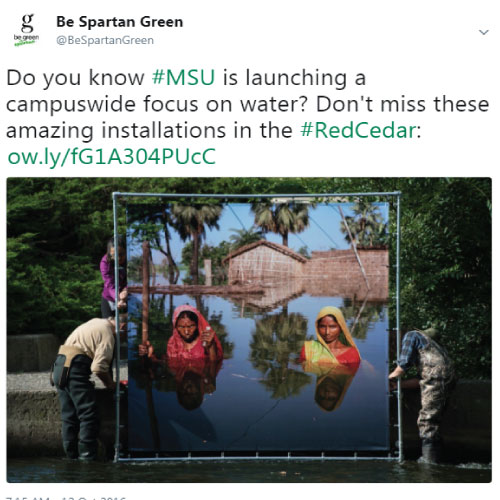 A screenshot of a tweet from @BeSpartanGreen, displaying a photo of the installation of Gideon Mendel's "Drowning World" exhibit being placed in the Red Cedar River.