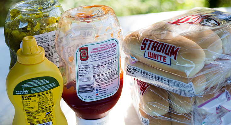 A photo of condiments and hot dog buns in bulk containers.