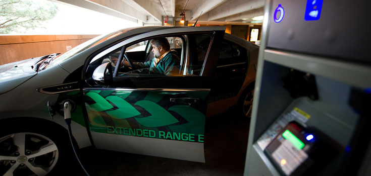 A close-up of a person using one of MSU's electric car charging stations. The electric nozzle plugs into the car's charging port.